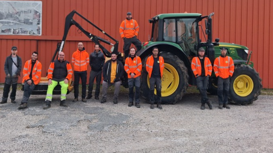 Équipe des Espaces Paysagers de Cahors réunie devant un tracteur et du matériel professionnel, illustrant le développement de l’activité, l’engagement des collaborateurs et les nouveaux moyens déployés par YMCA Services Occitanie.